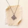 Stamped silver cross on oxidized silver chain necklace styled on tan linen.