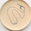 The still i rise bar necklace styled on a tan plate to show the adjustable lobster clasp closure