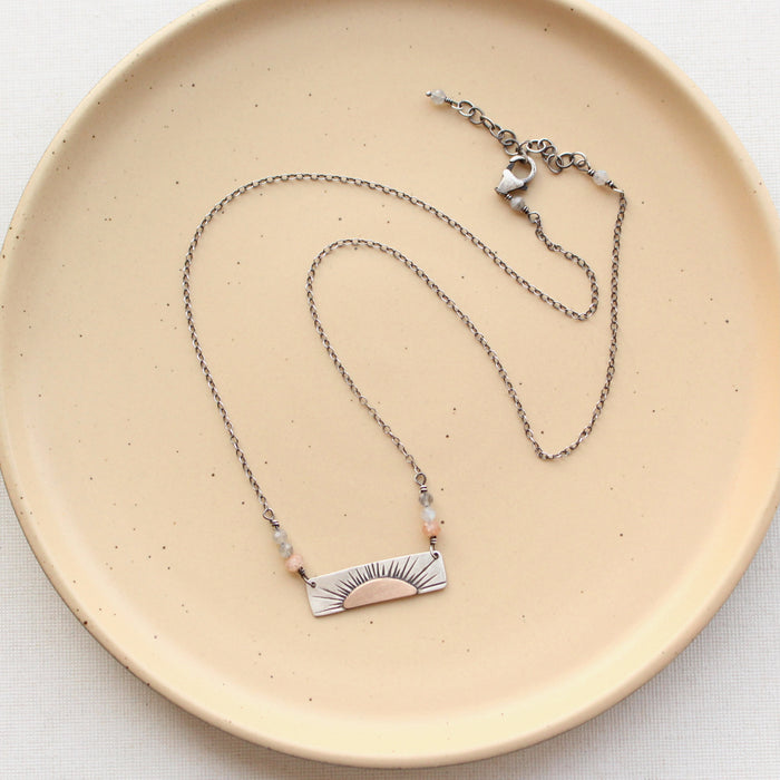 The still i rise bar necklace styled on a tan plate to show the adjustable lobster clasp closure
