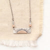 Horizontal bar necklace with bronze sun and sterling silver, with sunstone and labradorite, styled on tan linen.