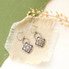 The talara bloom earrings styled on tan linen with dried grass
