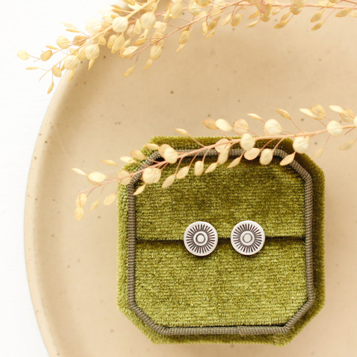 The talara sun post earrings styled on a green velvet box with dried grass