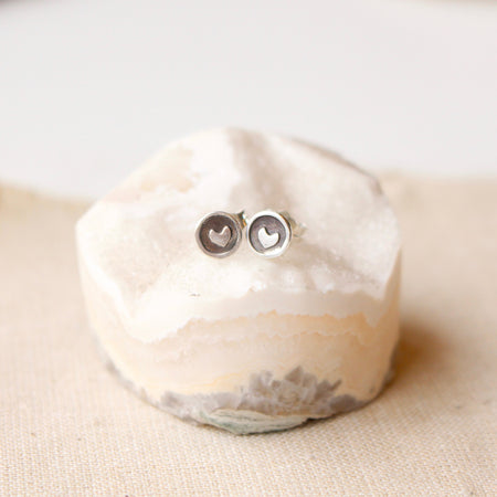 The teeny tiny heart post earrings styled on a rock with tan linen
