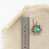 A turquoise jolie earring next to a ruler for size reference