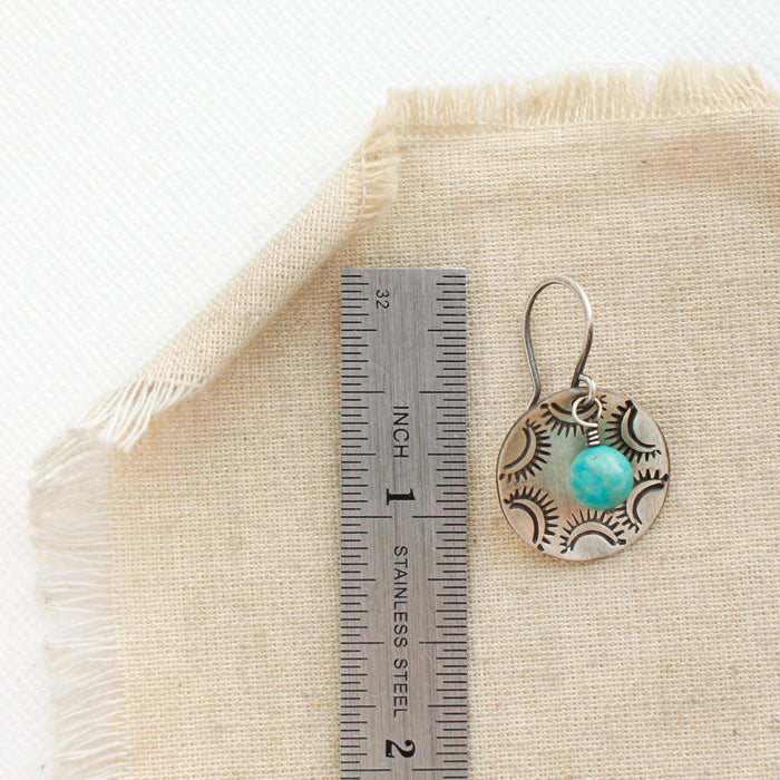 A turquoise jolie earring next to a ruler for size reference