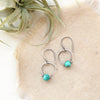 The turquoise la cloche earrings styled on tan linen with an air plant
