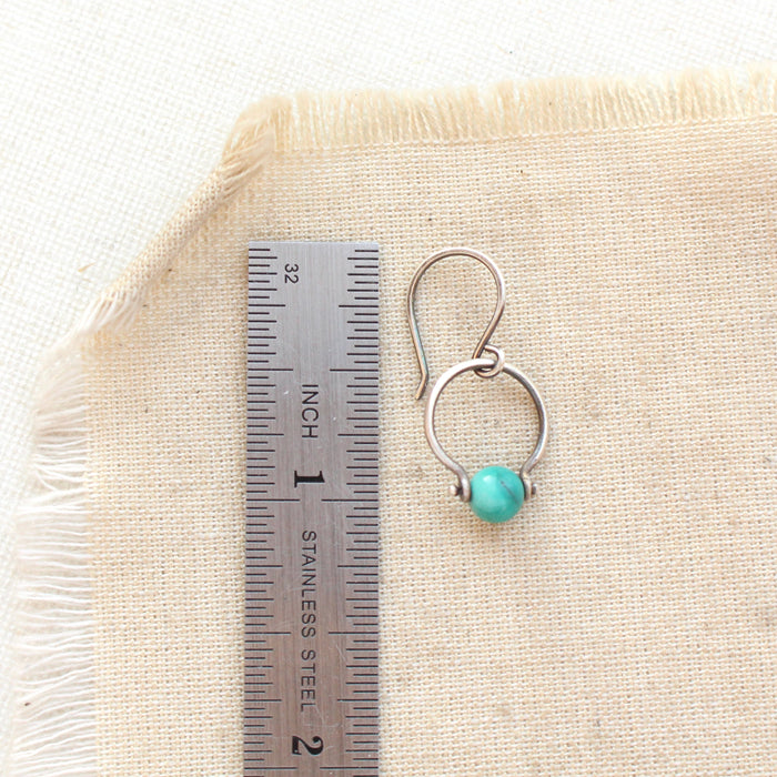 A turquoise la cloche earring next to a ruler for size reference