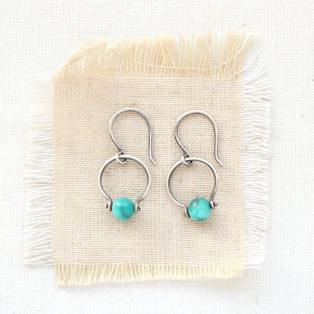The turquoise la cloche earrings styled on tan linen