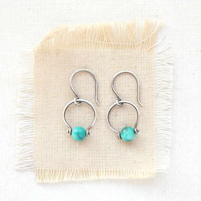 The turquoise la cloche earrings styled on tan linen