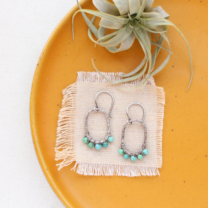 The turquoise wrapped hoop earrings styled on a yellow plate with linen and an air plant