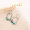 The turquoise wrapped hoop earrings styled on tan linen with dried grass