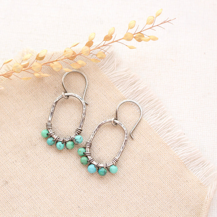 The turquoise wrapped hoop earrings styled on tan linen with dried grass