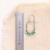 A turquoise wrapped hoop earring next to a ruler for size reference