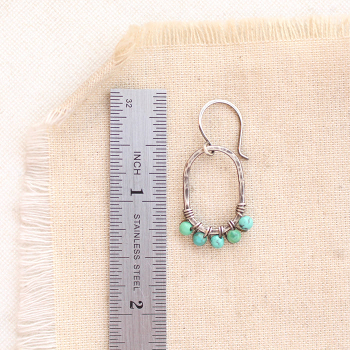 A turquoise wrapped hoop earring next to a ruler for size reference