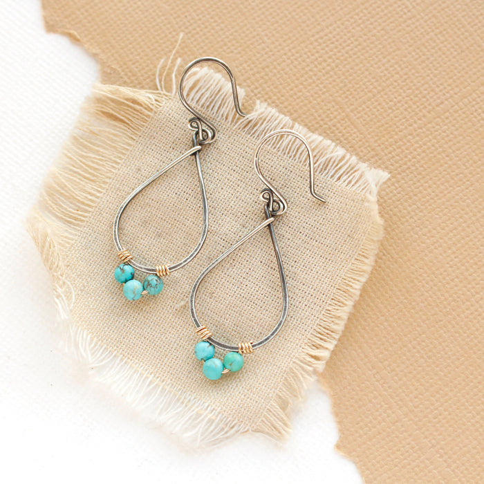 The turquoise wrapped teardrop hoop earrings styled on tan linen