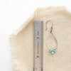 A turquoise wrapped teardrop hoop earring next to a ruler for size reference