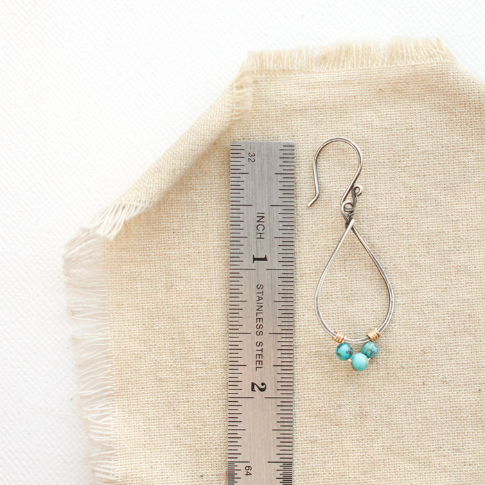 A turquoise wrapped teardrop hoop earring next to a ruler for size reference