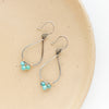The turquoise wrapped teardrop hoop earrings styled on a tan plate