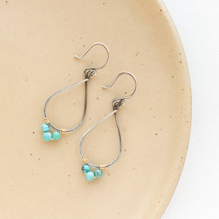 The turquoise wrapped teardrop hoop earrings styled on a tan plate