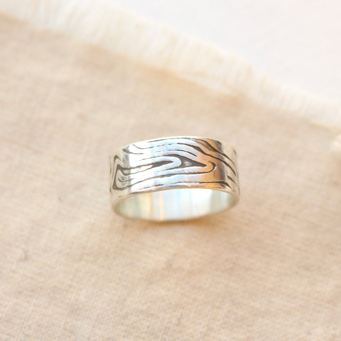 The woodgrain texture band ring styled on tan linen