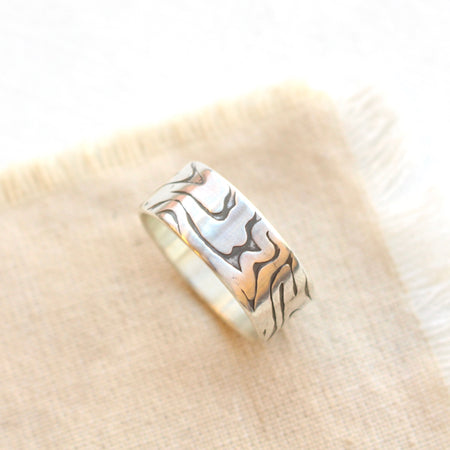 Woodgrain texture silver band ring styled on tan linen. 